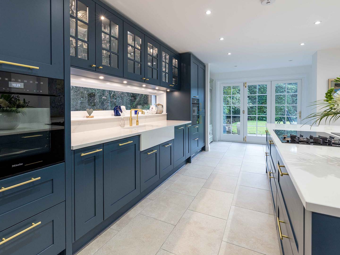 Blue Callerton kitchen cupboards, gold featured handles and white marble worktops paired with white sink
